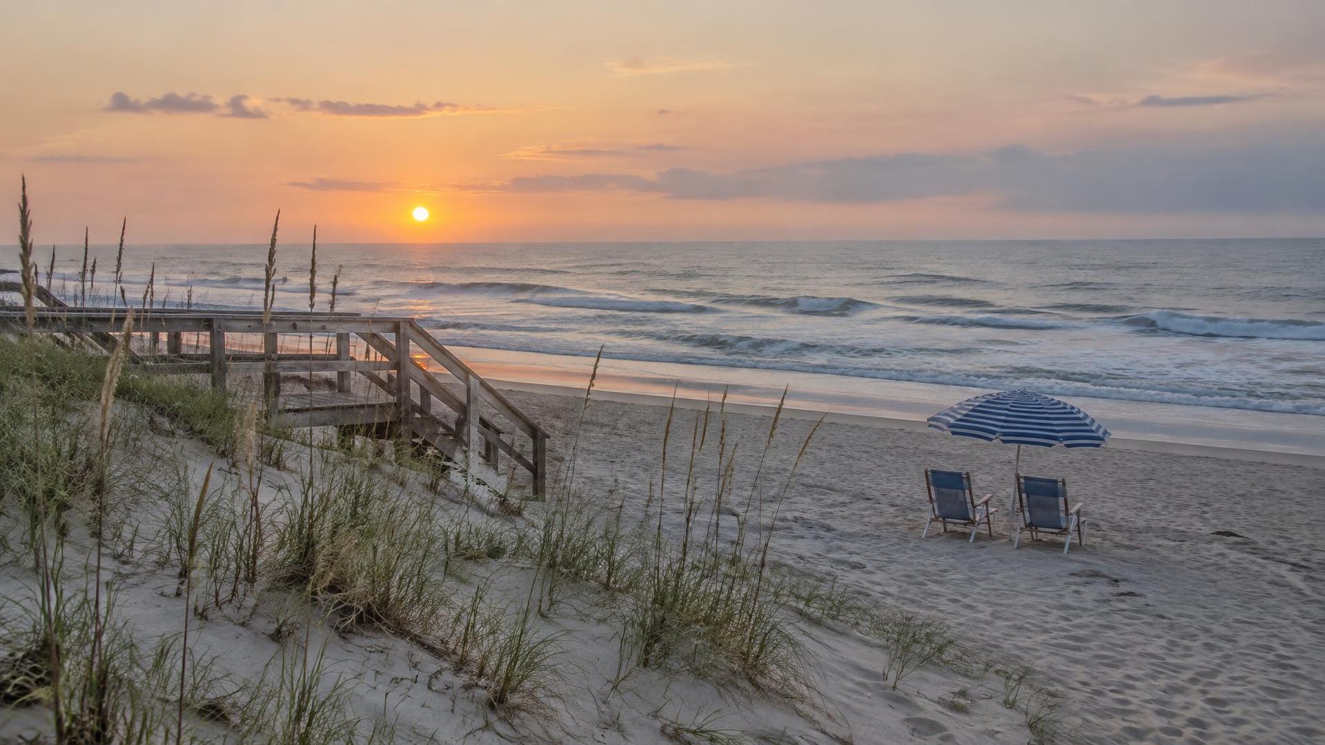 Sunrise over an Avon NC beach with sea oats, a dune walkway, chairs and an umbrella