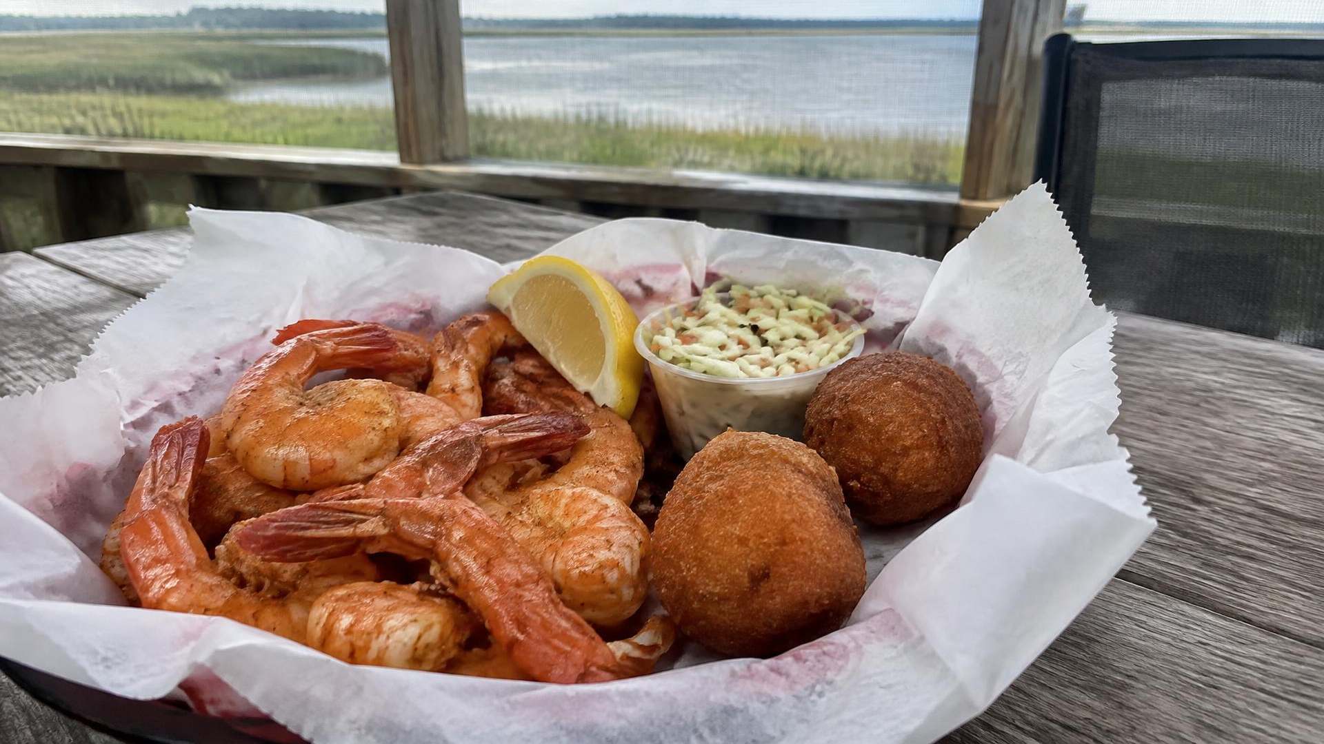 Basket of steamed shrimp, hush puppies and coleslaw on a screened porch overlooking the sound