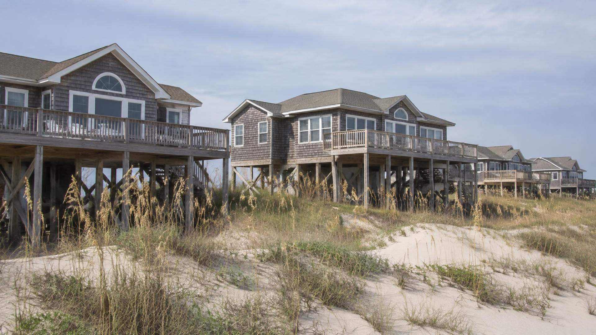 Elevated beach houses with ocean-facing decks behind low dunes in Avon NC