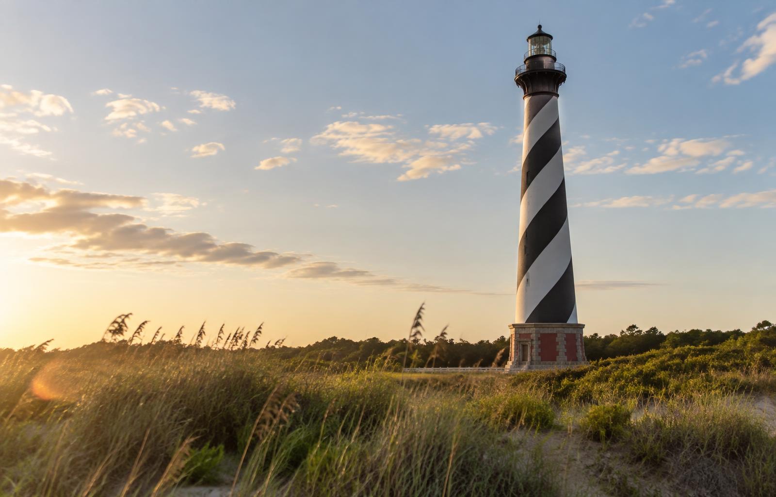 Black and white spiral-striped Cape Hatteras Lighthouse rising above dune grass at golden hour in Buxton on Hatteras Island, Outer Banks North Carolina